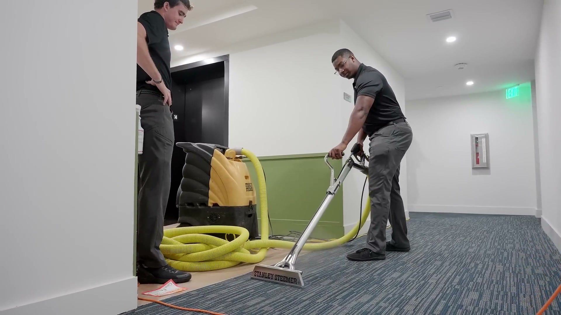 Stanley Steemer of South Florida technicians extracting carpet in a condo corridor